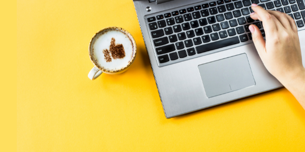 computer and cup of coffee on yellow background